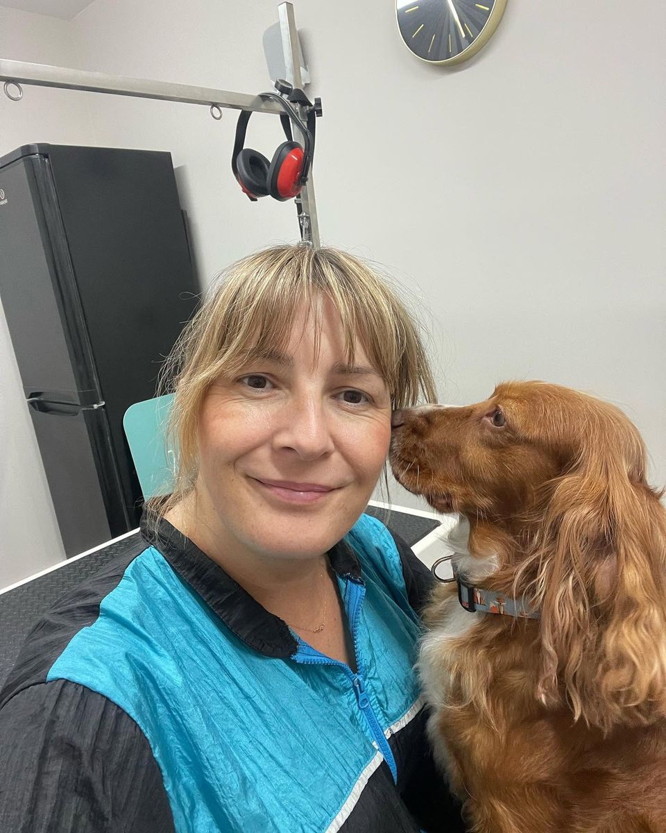 Magda smiling as a red cocker spaniel sniffs her cheek at Kiss My Mutt, Stone